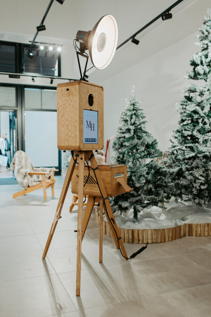Apres ski style photo booth at Cotswolds Designer Outlet with skis, faux snow and cosy winter decor, with the Christmas shopping centre photobooth , a wooden photo booth rental , Mad Hat Photo Booth