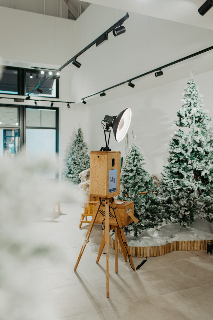 Apres ski style photo booth at Cotswolds Designer Outlet with skis, faux snow and cosy winter decor, with the Christmas shopping centre photobooth wooden Icon rental , Mad Hat Photo Booth