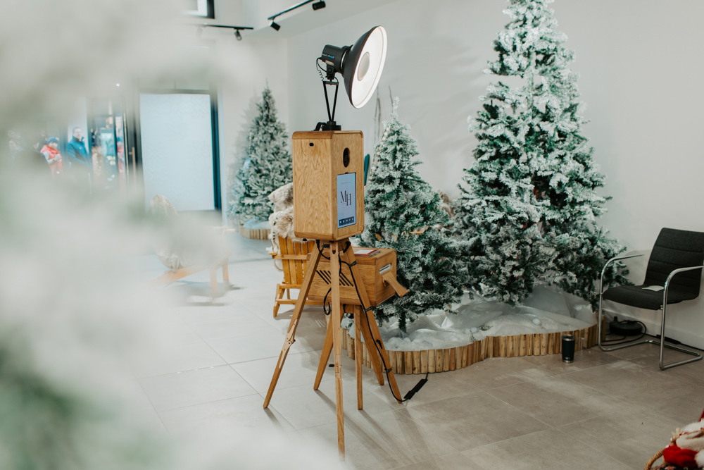Wide shot of apres ski photo booth zone at Cotswolds Designer Outlet showing backdrop, props and christmas tree with icon wooden photo booth hire
