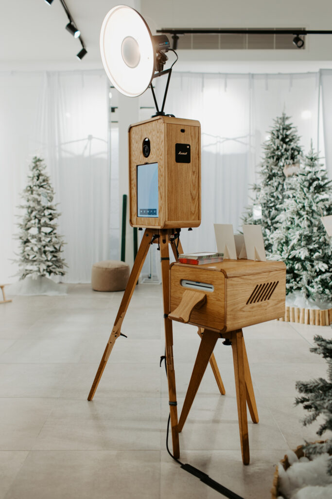 Apres ski style photo booth at Cotswolds Designer Outlet with skis, faux snow and cosy winter decor, with the wooden photo booth rental , Mad Hat Photo Booth