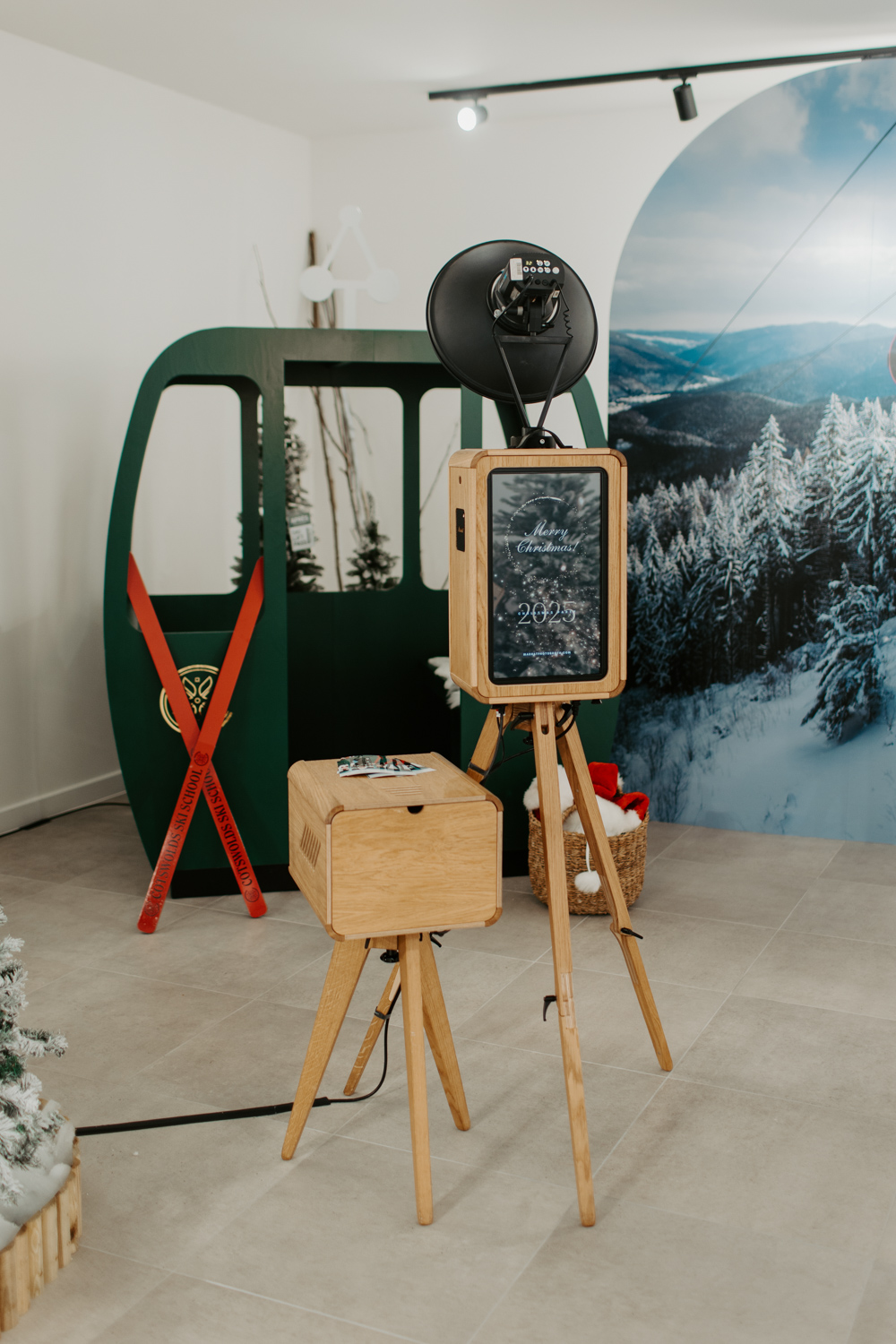 Apres ski style photo booth at Cotswolds Designer Outlet with skis, faux snow and cosy winter decor, with a Christmas shopping centre photobooth the wooden photo booth rental , Mad Hat Photo Booth
