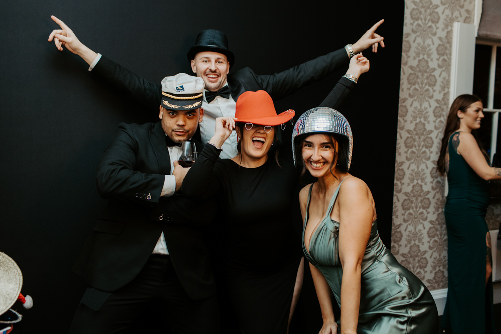 Team of guests in formal wear posing together for a photo booth picture at a black backdrop corporate Christmas celebration.