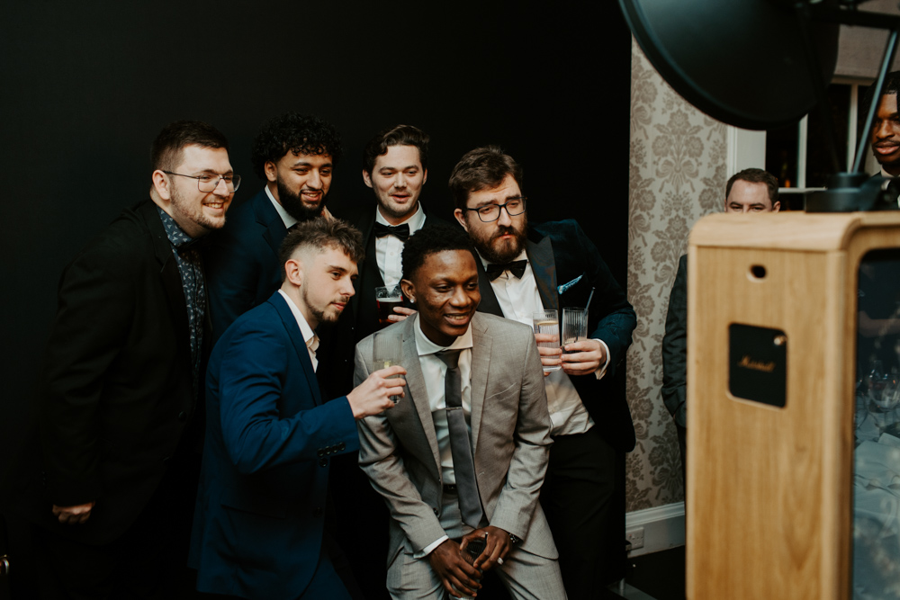 Guests laughing and posing in front of a black backdrop during a Christmas corporate party, wearing fun festive props.