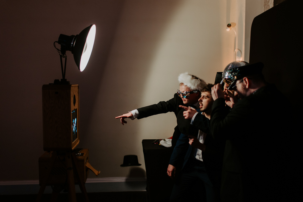 Team of guests in formal wear posing together for a photo booth picture at a black backdrop corporate Christmas celebration.