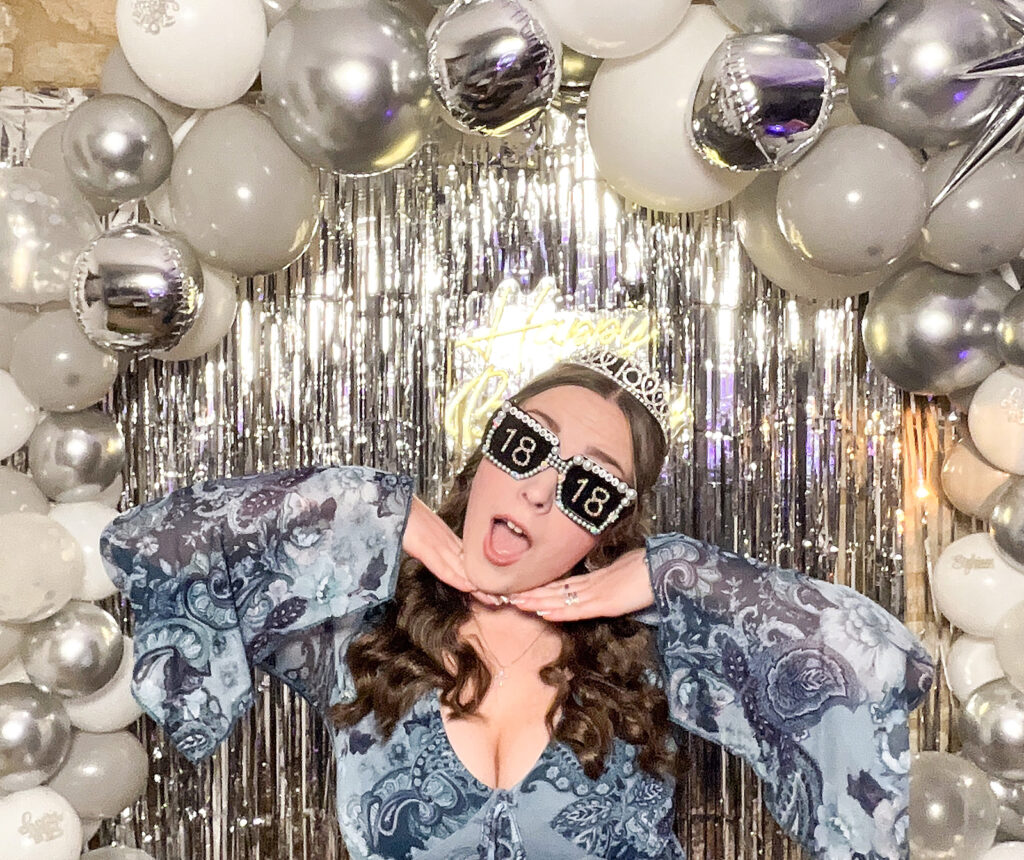girl posing against a silver backdrop with balloons for her 18th birthday party for the best cheltenham selfie pod rental
