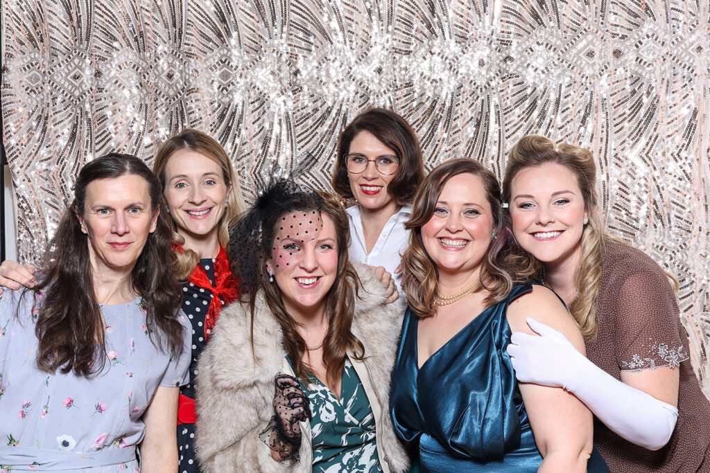 group of friends dressed up for an 1940s birthday party theme, with a sequins backdrop on the back, for a 40th birthday celebration