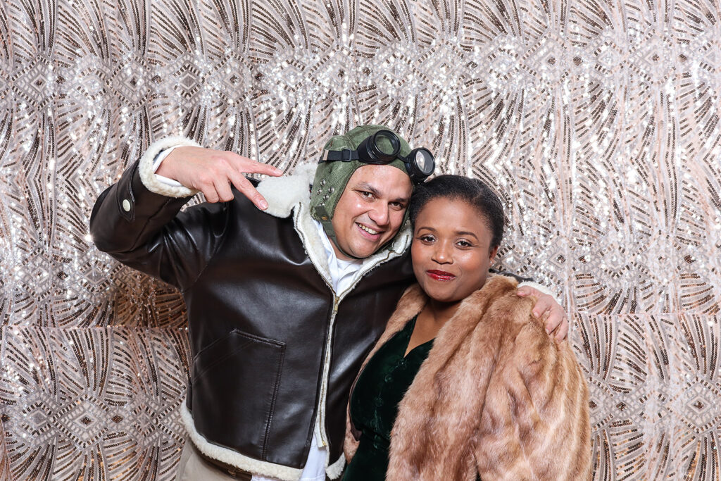 2 guests dressed up for an 1940s party theme, with a sequins backdrop on the back with mad hat photo booth hire