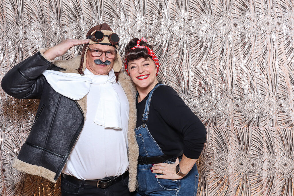 2 guests dressed up in an 1940s outfit posing against a sequins boho backdrop, during a birthday party photo booth rental
