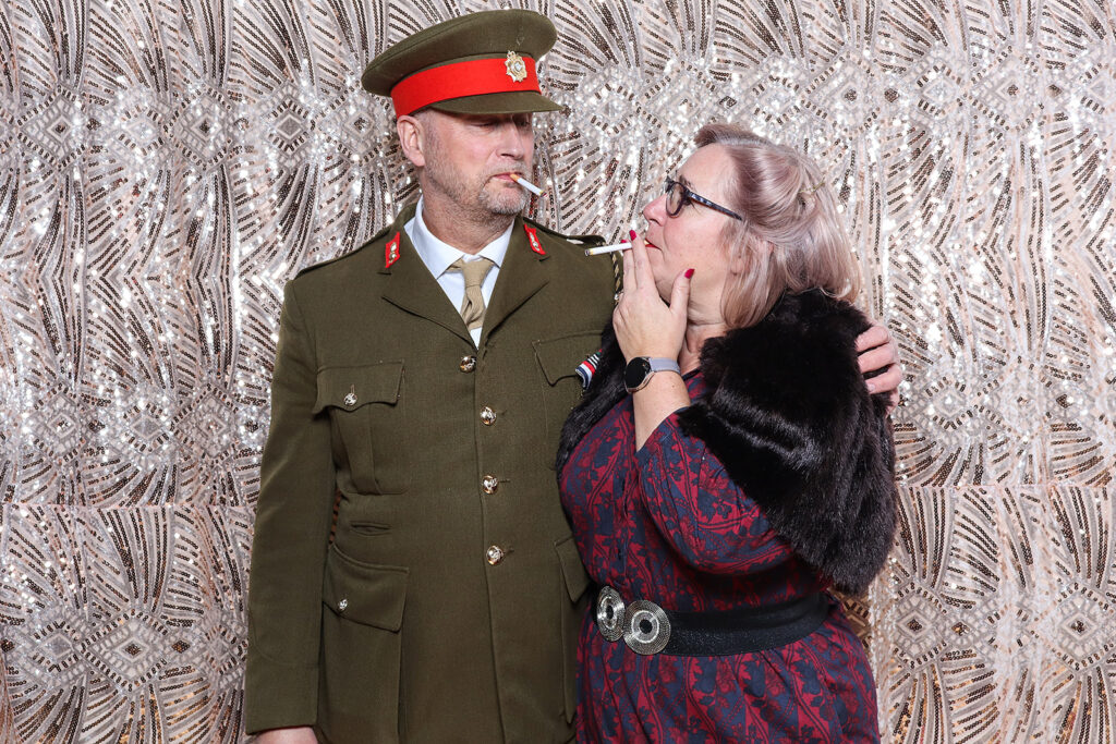 2 guests dressed up in an 1940s outfit posing against a sequins boho backdrop, during a birthday party photo booth rental
