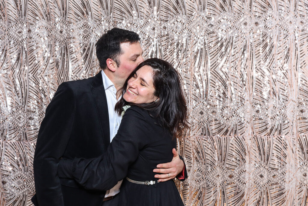 2 guests hugging, dressed up posing against a sequins boho backdrop, during a birthday party photo booth hire cheltenham

