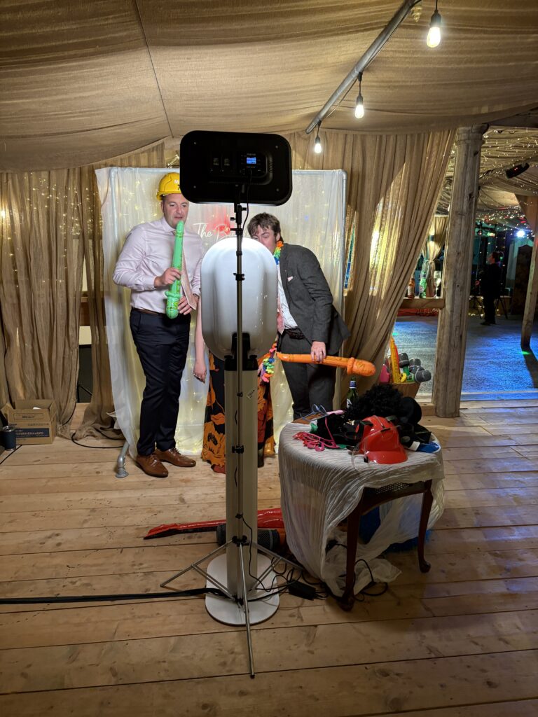 guests posing for a selfie pod rental setup during a very intimate wedding with a custom white backdrop and a few props on a small round table next to the pod
