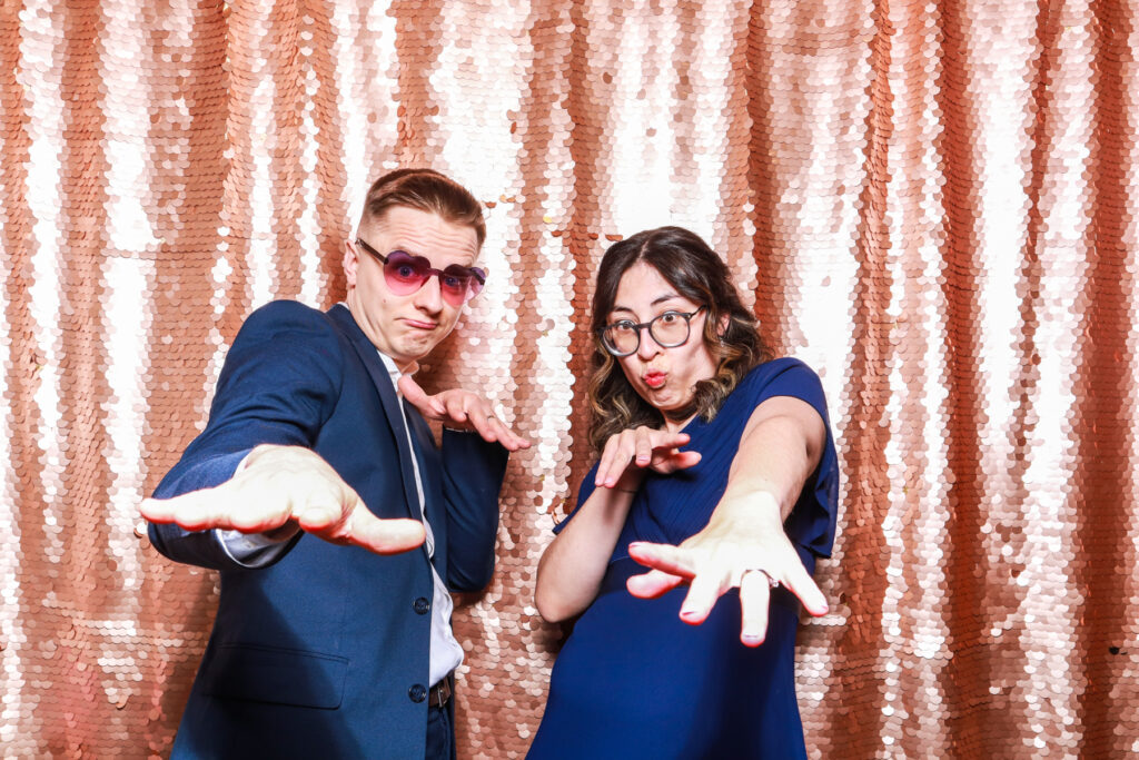 2 guests posing silly against a sequins backdrop for mad hat photo booth, cotswolds booth for weddings and events
