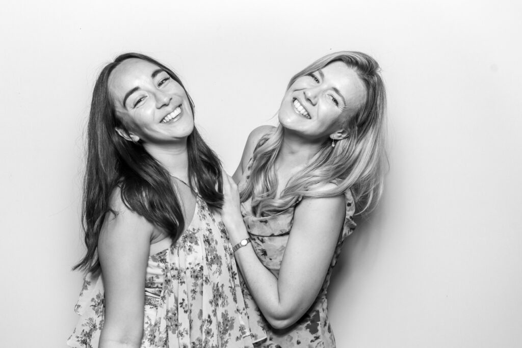 black and white image from a party entertainment with 2 girls posing for photobooths for events, with a white backdrop 
