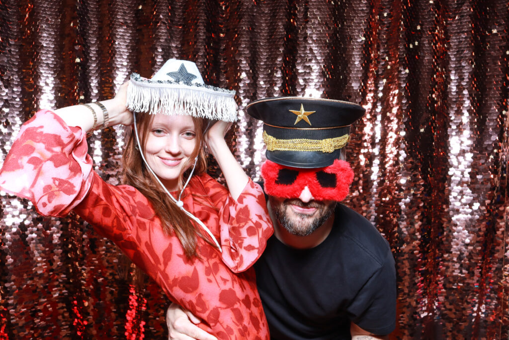 couple posing for a photobooths for events hire in the cotswolds, with party props and sequins backdrop 


