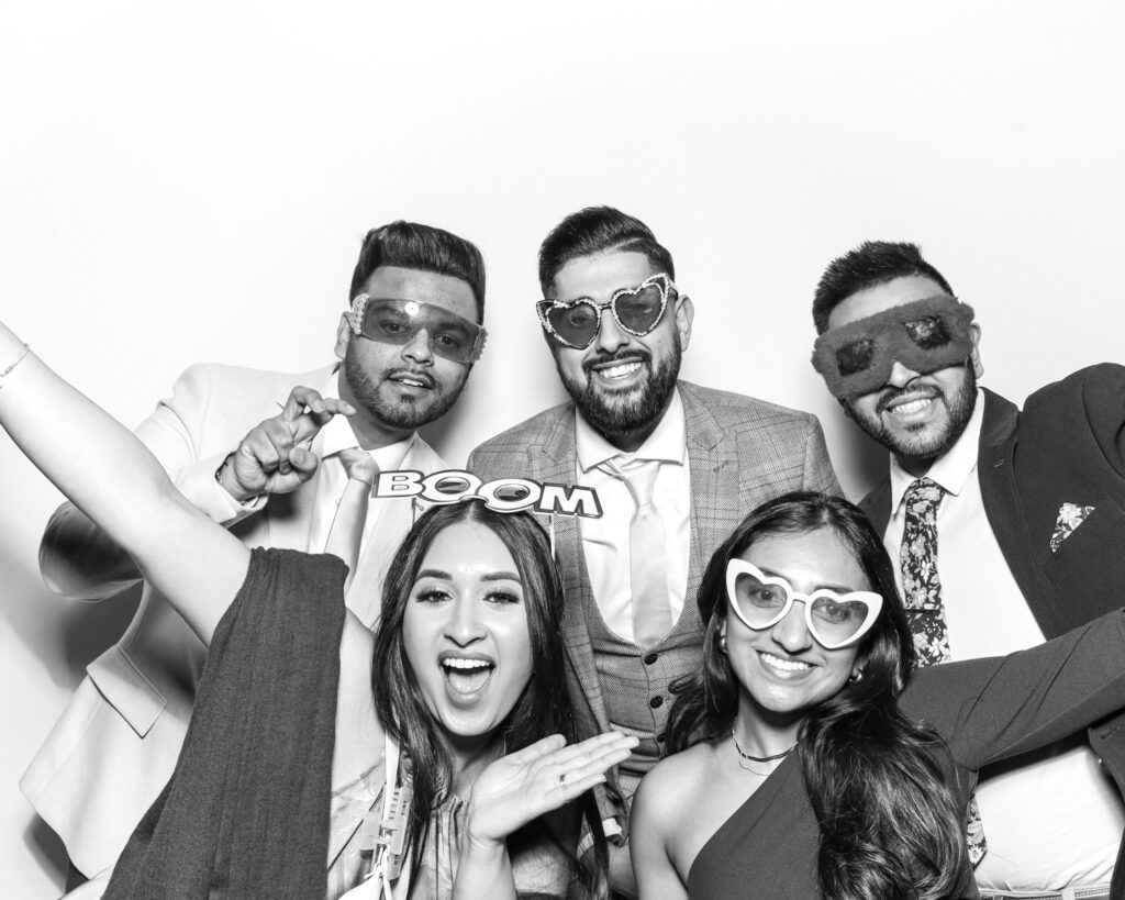 black and white photo from a corporate party entertainment with 5 guests wearing props, posing against a white backdrop 
