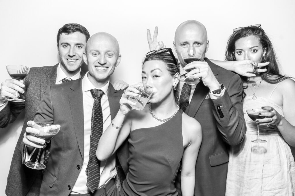 black and white photo from a corporate party entertainment with 5 guests wearing props, posing against a white backdrop 

