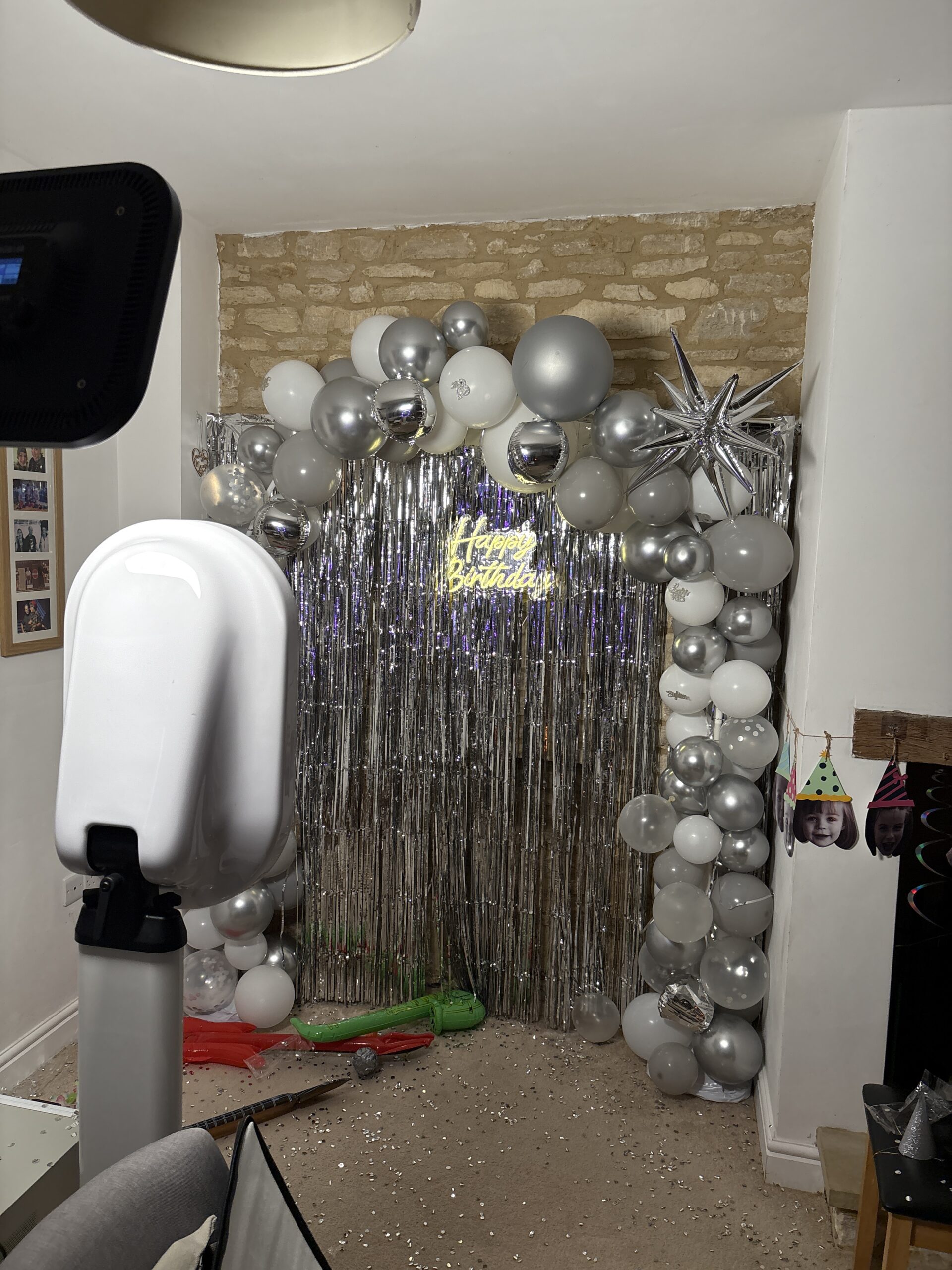 Ipad booth selfie pod rental setup for an 18th birthday party with a custom silver backdrop with balloons and a few inflatable props on the floor
