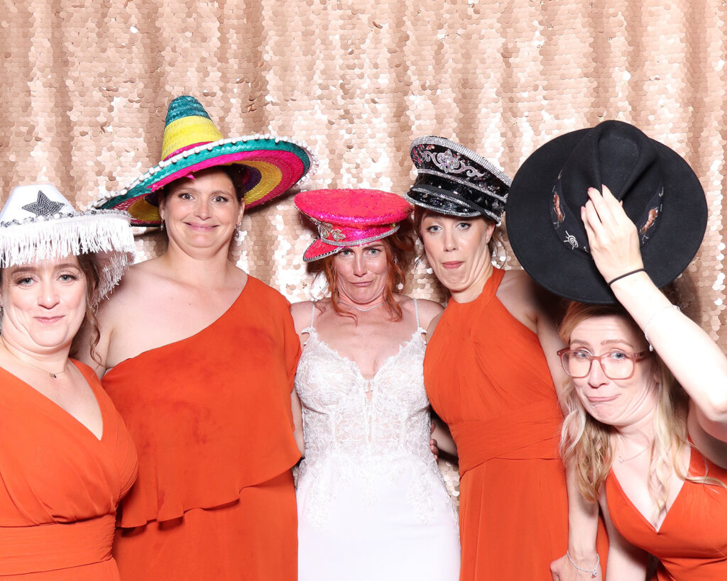 4 ladies and a bride dressed in red and orange with a blush sequins backdrop for a De Vere Tortworth Court Wedding photo booth hire

