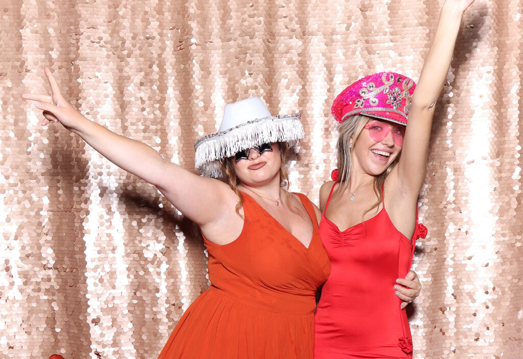2 ladies dressed in red and orange with a blush sequins backdrop for a De Vere Tortworth Court Wedding photo booth hire
