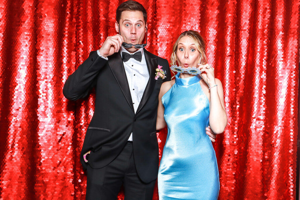 couple posing against a red bright backdrop for a Wedding Photo Booth with Props during a wedding party entertainment
