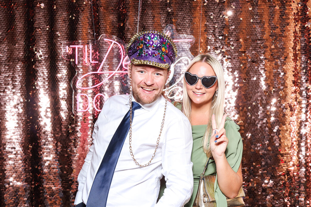 couple posing a champagne sequins backdrop with lots of fun festival props, for a wedding photo booth hire
