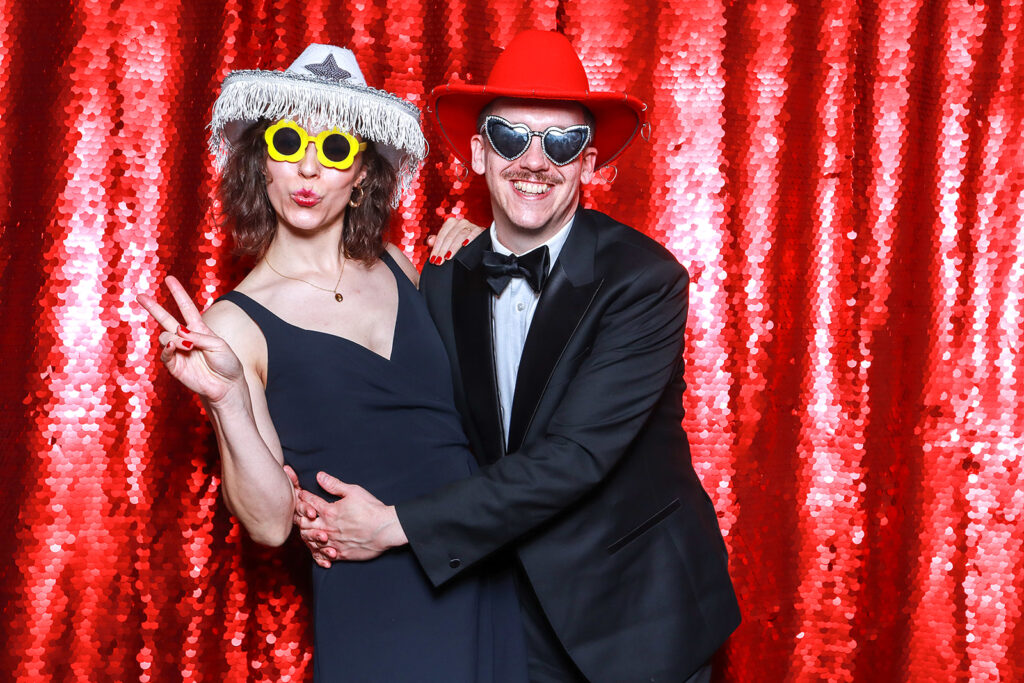 couple posing against a red bright backdrop for a Wedding Photo Booth with Props during a wedding party entertainment