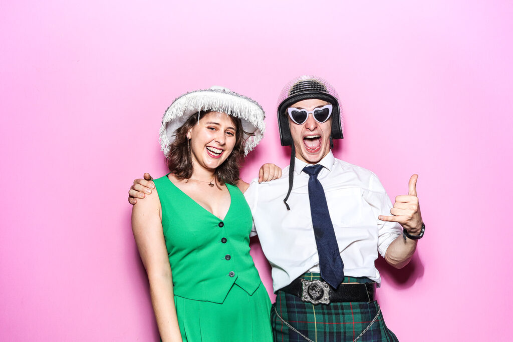 couple posing against a bright bubble pink backdrop for a Wedding Photo Booth with festival Hat Props during a wedding party entertainment