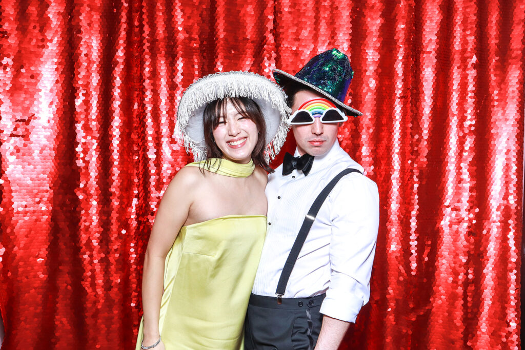 couple posing against a red bright sequins backdrop for a Wedding Photo Booth with Props during a wedding party entertainment