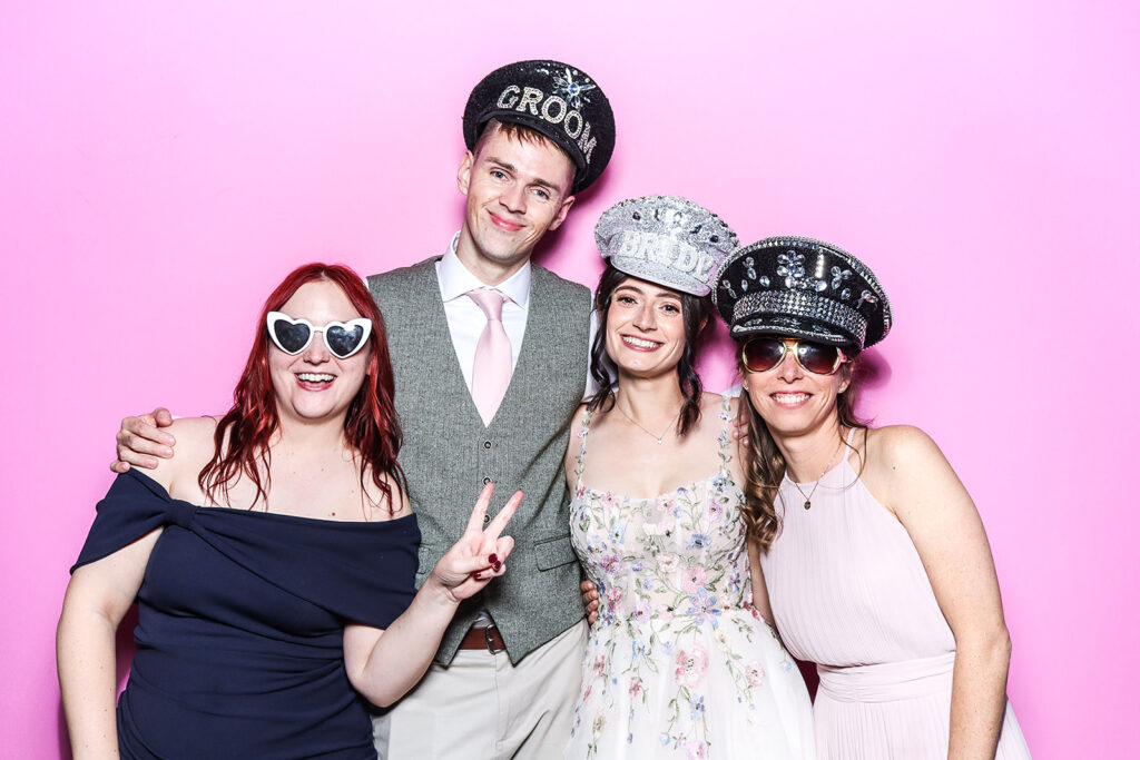 guests posing against a bright bubble pink backdrop for a Wedding Photo Booth with festival Hat Props during a wedding party entertainment