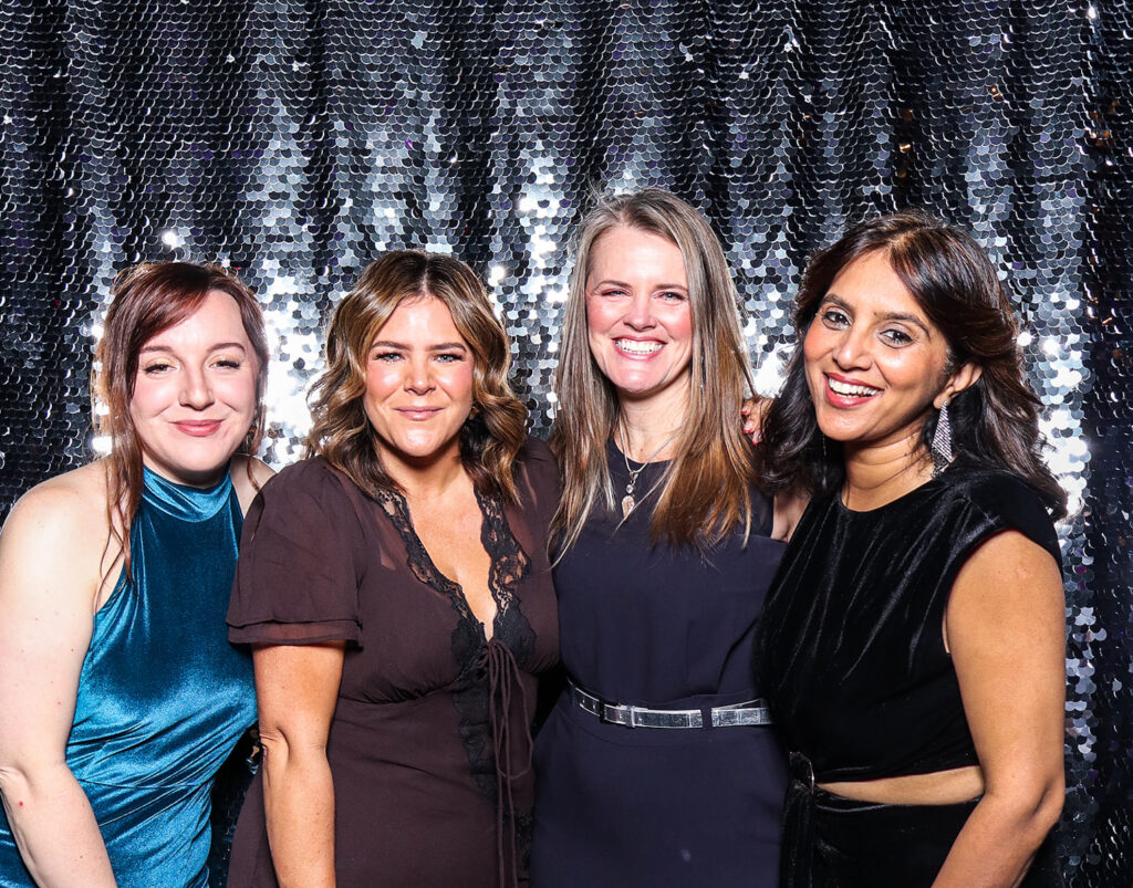4 guests dressed elegantly during a Charity Gala Photo Booth Hire event entertainment posing against a silver sequins backdrop for a corporate event