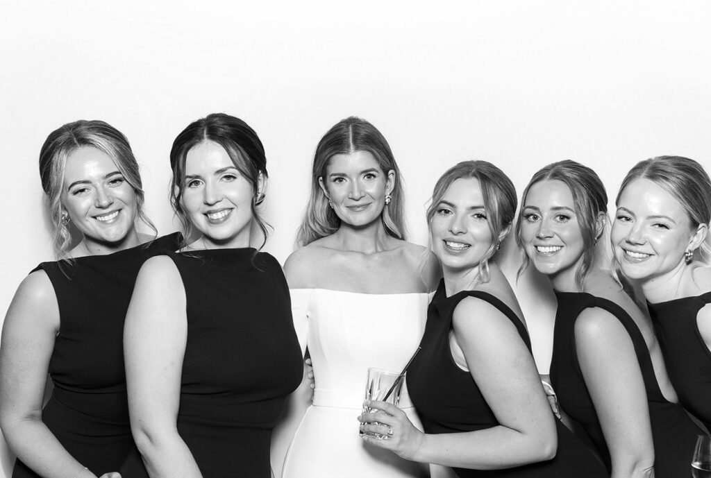 6 guests dressed elegantly during a Charity Gala Photo Booth Hire event entertainment posing against a white backdrop for a b&w image during a corporate event