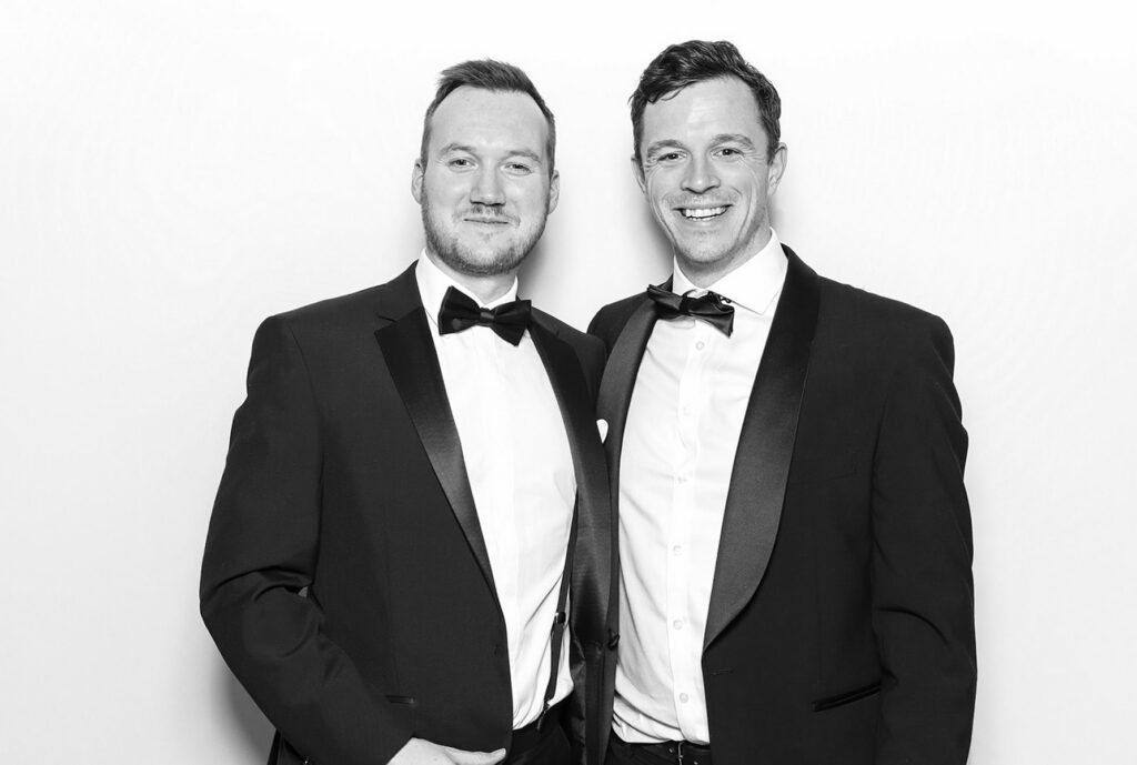 2 guests dressed elegantly during a Charity Gala Photo Booth Hire event entertainment posing against a white backdrop for a b&w image during a corporate event