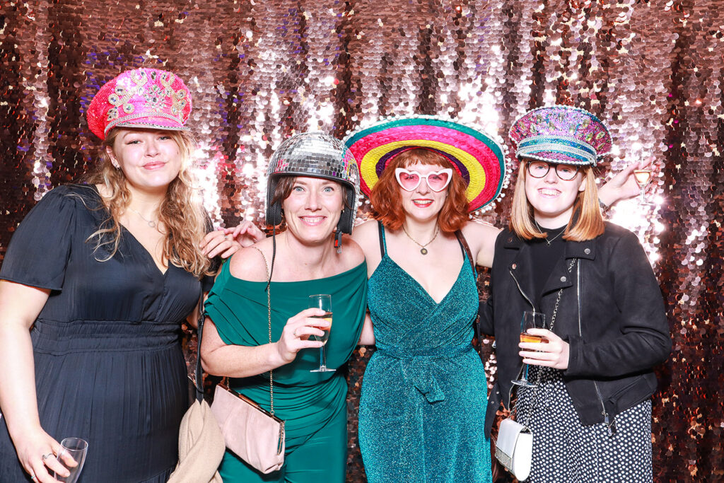 Luxury Corporate Photo Booth Rental in Oxfordshire with guests posing against a champagne sequins backdrop wearing fun props, during a ball room event