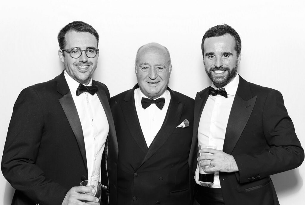 black and white image of 3 guests  posing against a white backdrop for an awards gala