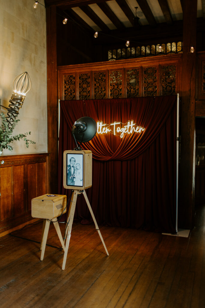 luxury wooden photo booth- the icon with a custom rear screen and wooden print box, in front of a burgundy drape backdrop with a "better together" neon sign hire for a wedding event around the cotswolds
