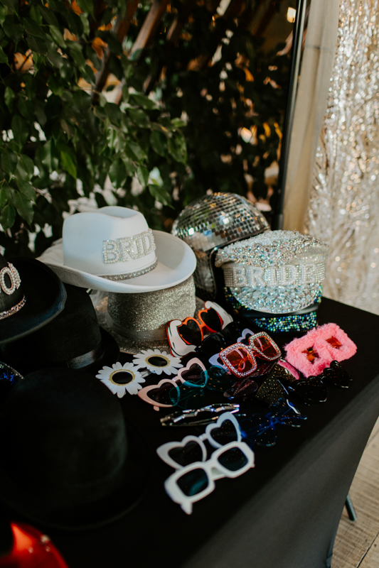 Fun wedding photo booth props and festival style props, arranged on a table beside a wooden booth