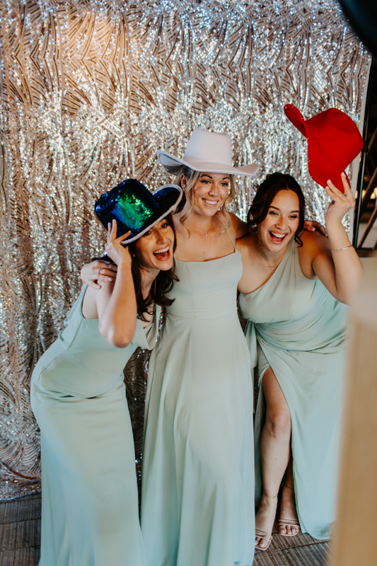 Guests having fun posing for a photo booth hire wit festival style props and a bohemian sequins backdrop
