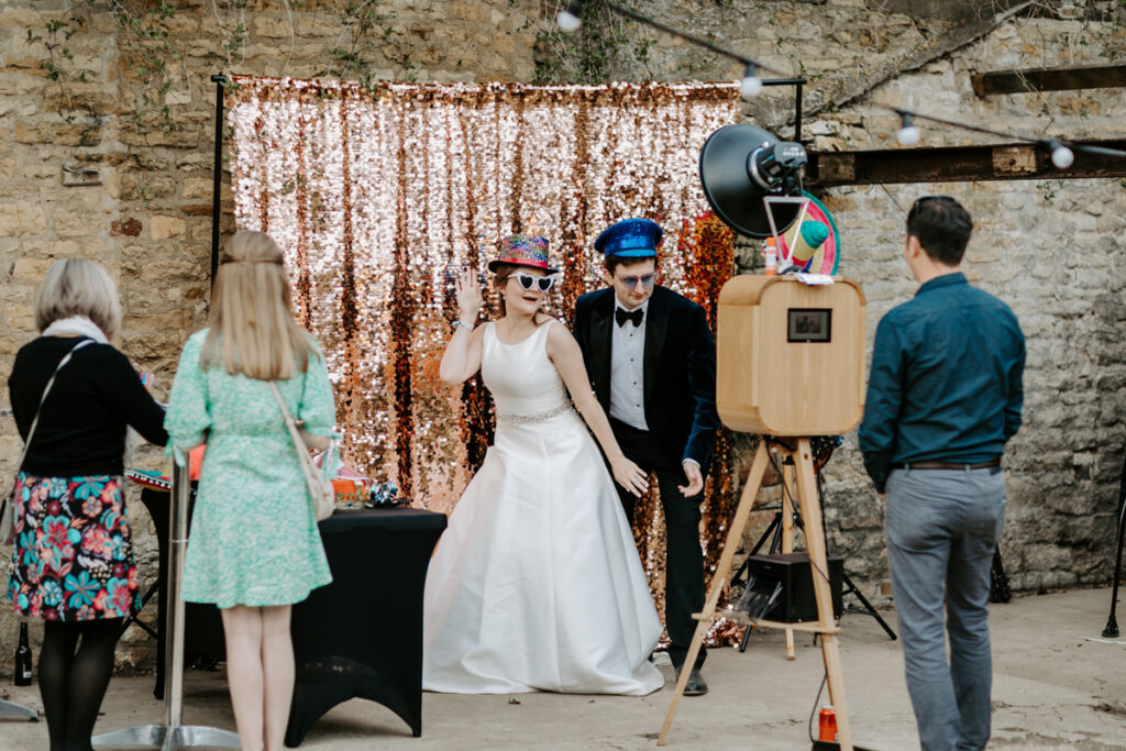 The Retro wooden photo booth at a rustic wedding venue with studio-quality prints during an outdoor reception, with the champagne sequins backdrop
