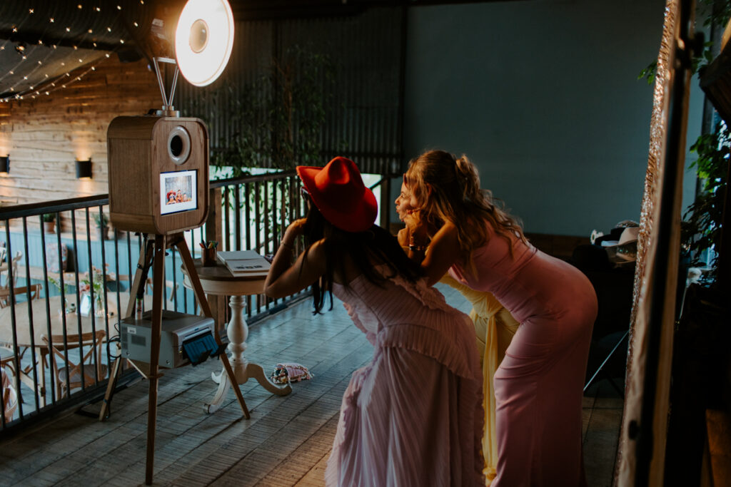 stone Barn wedding photo booth with a wooden booth and rustic barn backdrop and guests posing with party props