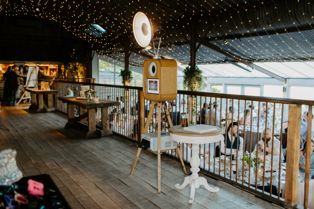 stone Barn wedding photo booth with a wooden booth and rustic barn backdrop and guests posing with party props