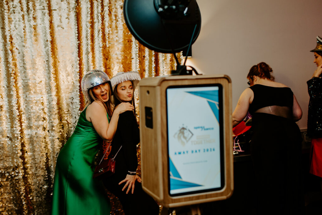 De Vere Cotswold Water Park Photo Booth Hire during a large corporate event, with guests posing against a gold shimmer backdrop

