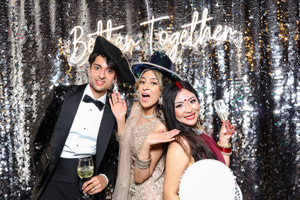 asian guests posing for a photobooth rental, against a silver  backdrop during a wedding reception entertainment in Wiltshire 