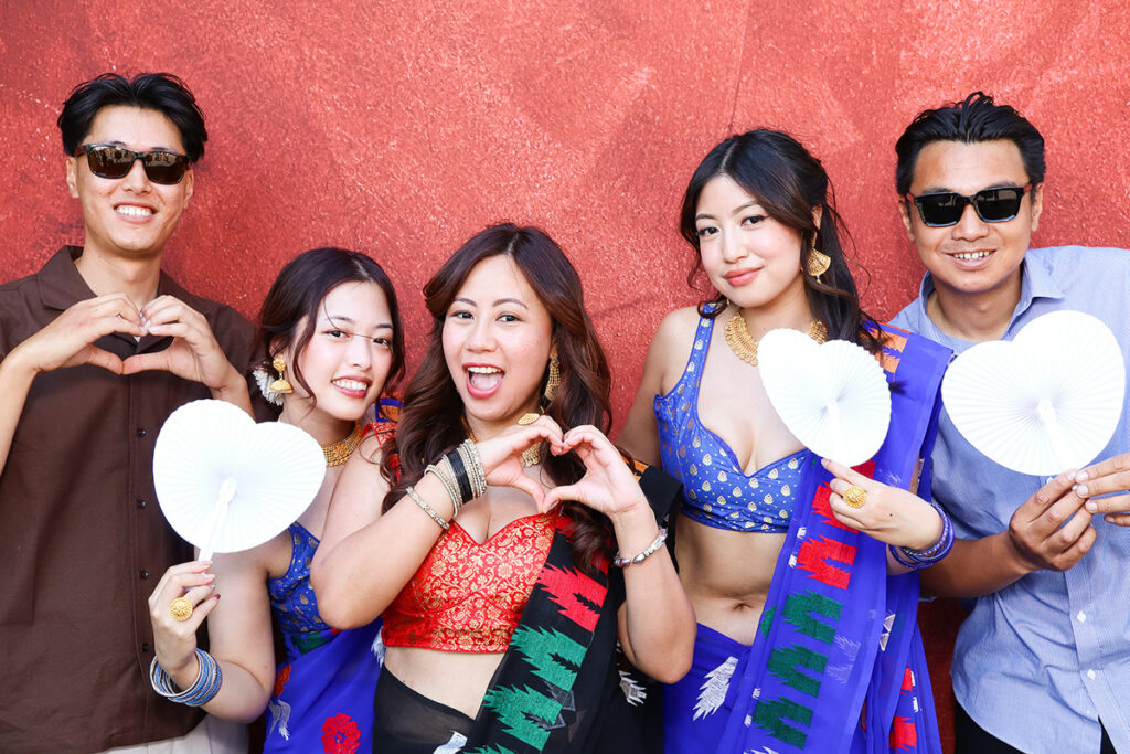 asian guests posing for a photo booth hire, against a maroon backdrop during a 2-day wedding party entertainment in Wiltshire 