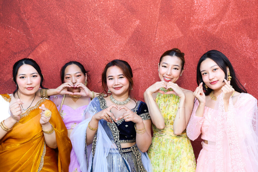 asian guests posing for a photo booth hire, against a maroon backdrop during a 2-day wedding party entertainment in Wiltshire 