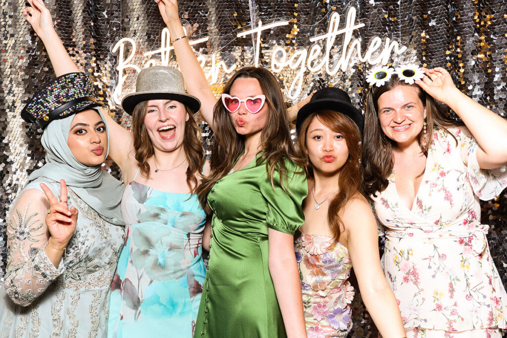 asian guests posing for a photobooth rental, against a silver  backdrop during a 2-day wedding reception entertainment in Wiltshire 