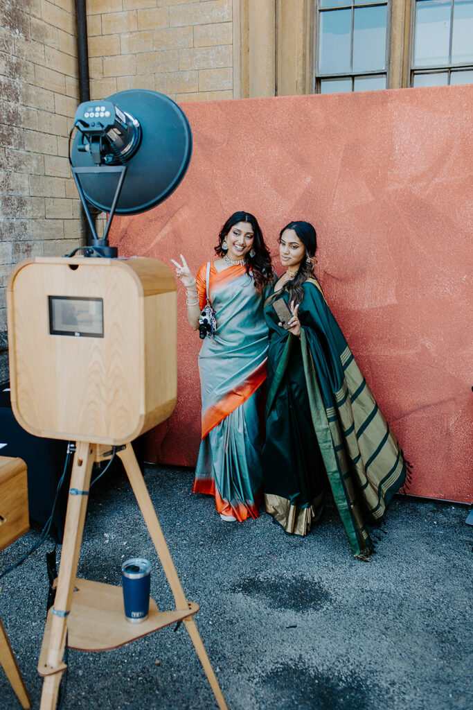 guests posing for a premium wooden photo booth setup with props, and maroon  backdrop for an outdoor garden party at Grittleton House wedding venue in Wiltshire 
