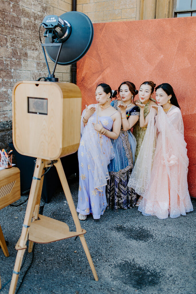 asian guests posing against a maroon backdrop during a 2-day wedding party entertainment at Grittleton House wedding venue