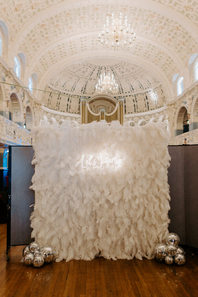 white feather backdrop with a Let's party neon sign and disco balls during a corporate event at Oxford Town Hall
