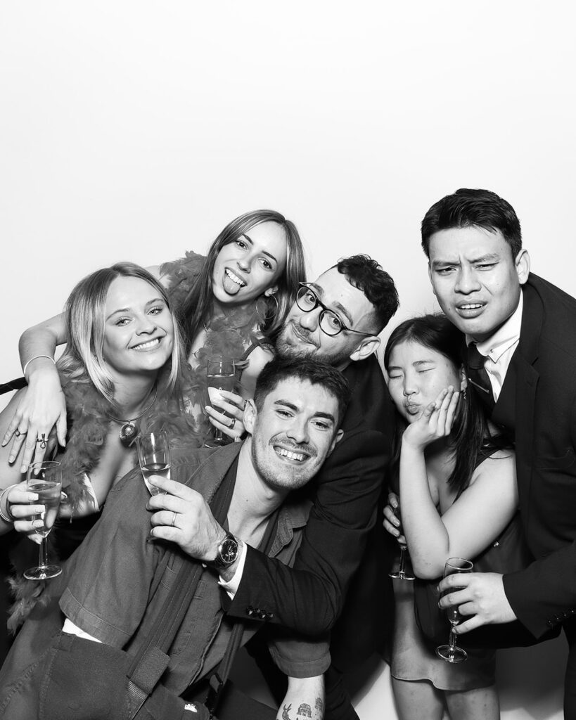 b&w image of large group of guests posing against a white backdrop, during a corporate event party entertainment with mad hat photo booth hire in oxfordshire