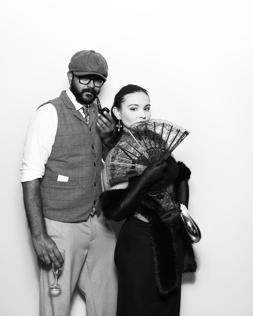 b&w image of couple wearing props posing against a white backdrop, during a corporate event party entertainment with mad hat photo booth hire in oxfordshire